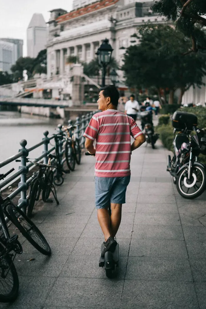 A man on an electric unicycle passes parked bicycles by a river, representing interactions that may lead to misunderstandings between locals and foreigners.