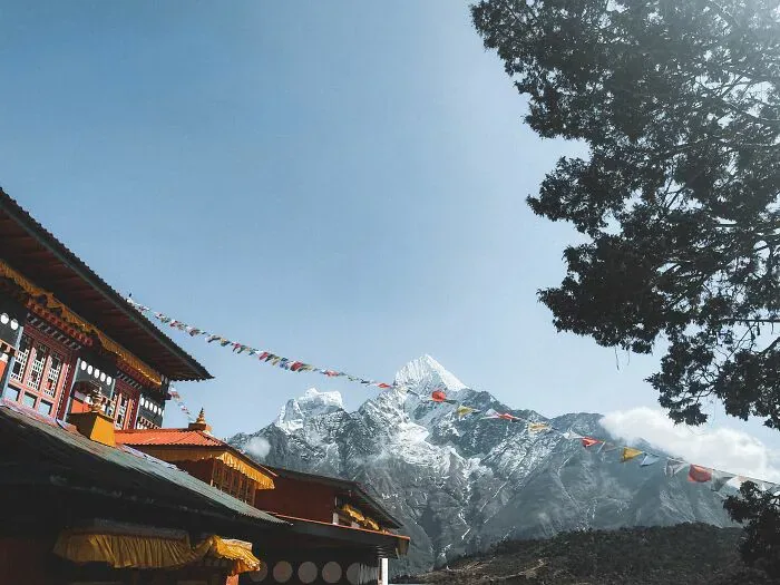 Buddhist monastery with prayer flags, a snow-capped mountain, and clear sky, representing locals and foreigners.