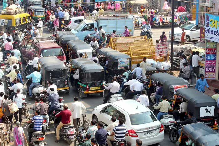 Busy Indian street with many auto-rickshaws, cars, and pedestrians, highlighting challenges for locals and foreigners.