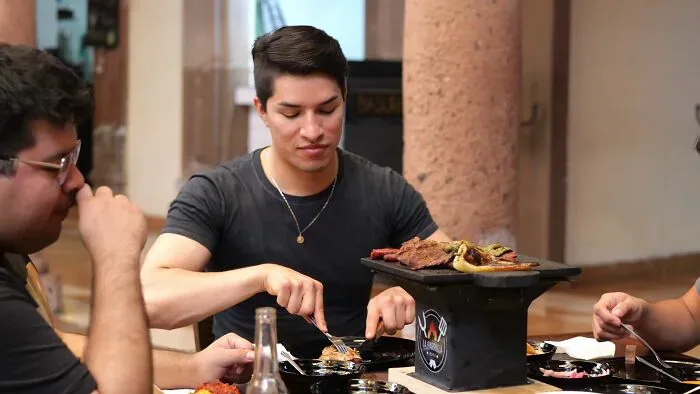 Young man grilling meat at his table with friends, a common activity for locals and foreigners.
